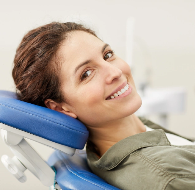 Smiling woman resting head on blue dental headrest in modern dental office setting.