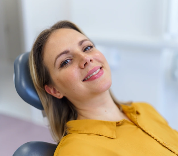 Woman in yellow shirt smiling in dental office chair during examination.